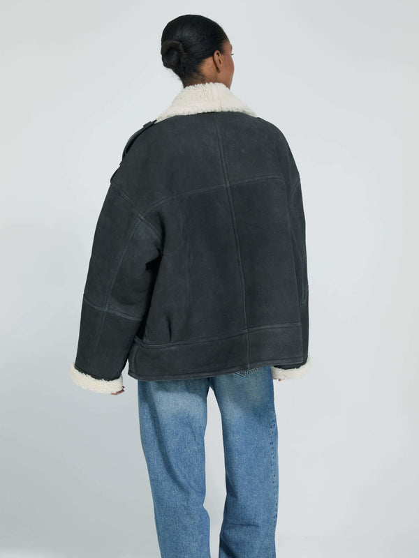 A model wearing a cozy, oversized black shearling jacket with a soft white collar, paired with relaxed blue jeans. MEOTINE.