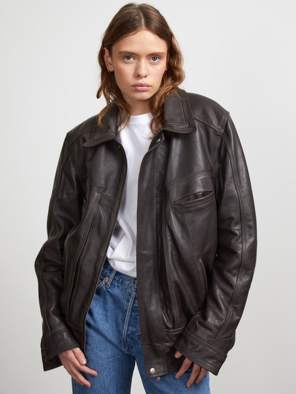 A model showcases a stylish brown leather jacket from MEOTINE, paired with a simple white t-shirt and blue jeans.