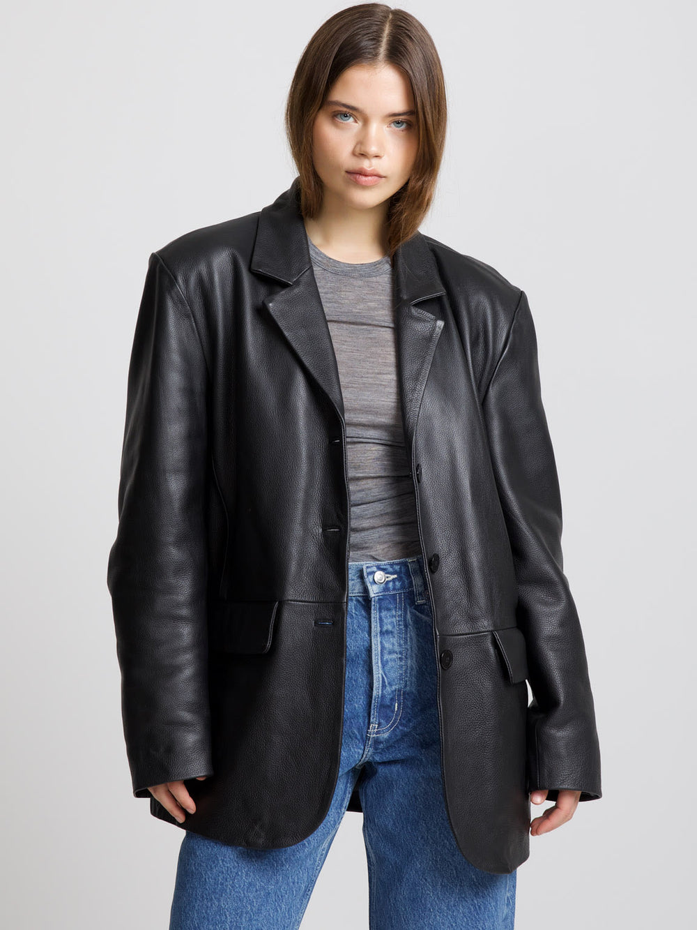 A model showcases a stylish oversized black leather blazer paired with a gray top and high-waisted jeans, embodying MEOTINE's chic aesthetic.