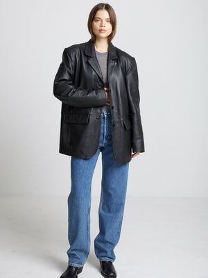 A model showcases a stylish black leather blazer paired with high-waisted blue jeans, embodying a chic MEOTINE look.