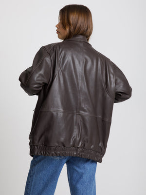 Brown leather jacket with a relaxed fit, featuring a high collar and elastic hem, styled with blue jeans. MEOTINE brand.