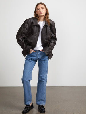 A model wearing a dark brown leather jacket over a white t-shirt, paired with light blue jeans and black shoes, showcasing MEOTINE style.